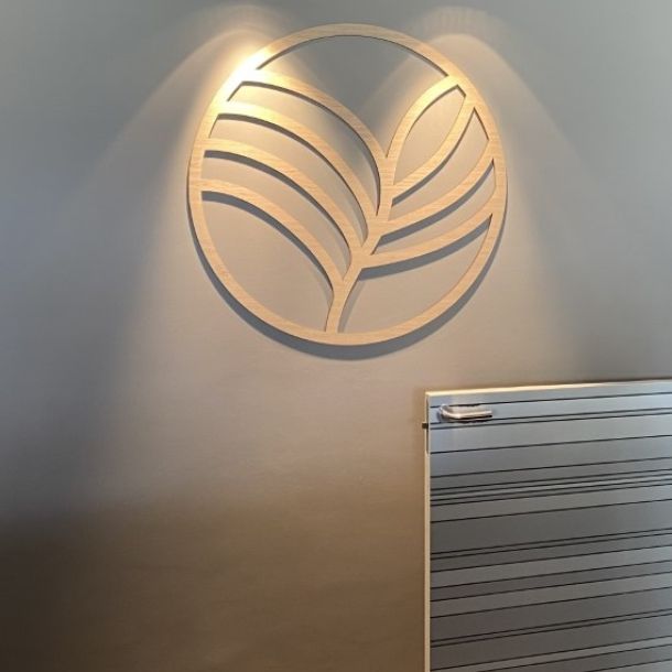 Rundt logo med mønster. Monteret i hotelreception. Træ i lys eg belyst fra loftet.