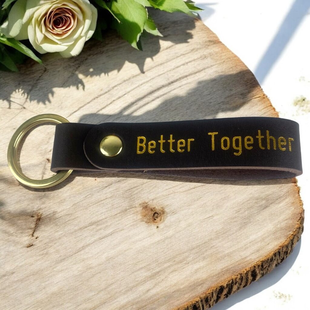 Brun lædernøglering med guld tryk. Der står Better Together. Ligger på et rustikt bord med en rose.