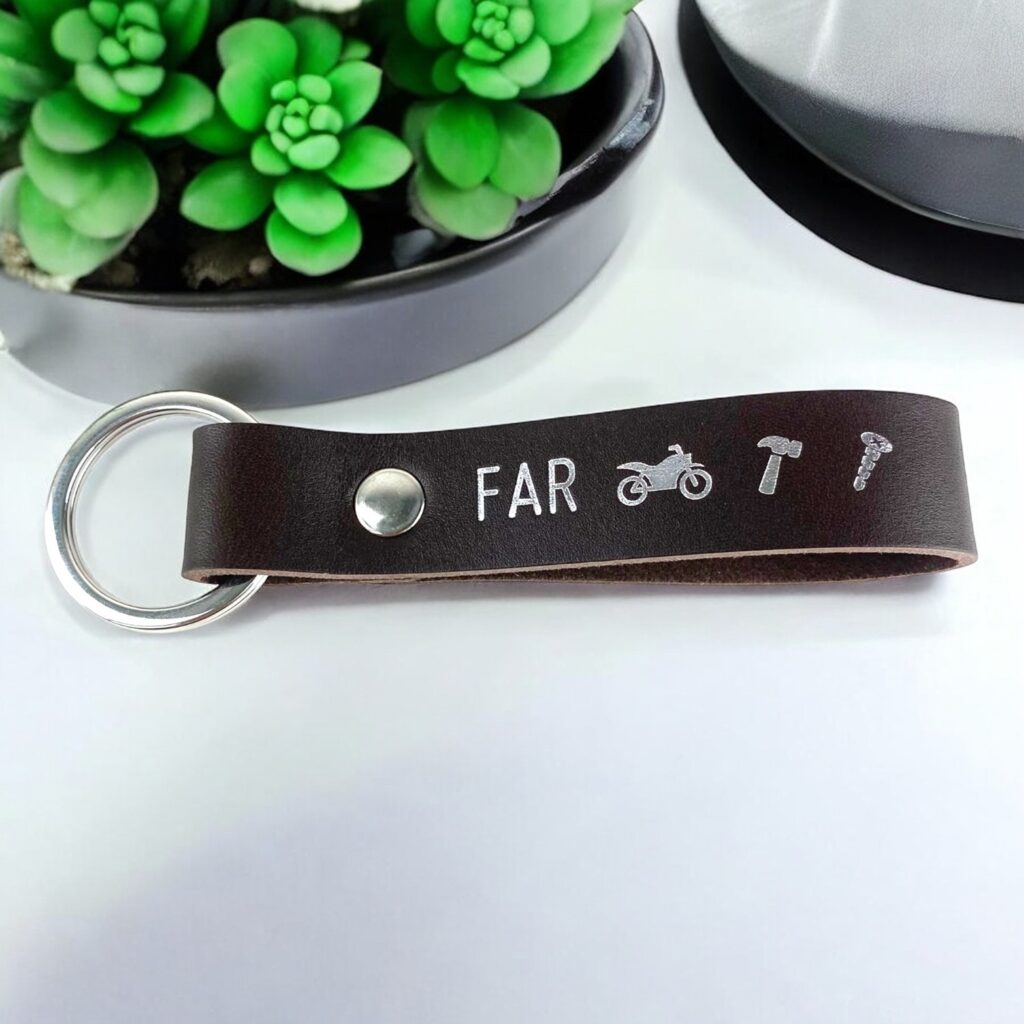 Brun lædernøglering med sølv tryk. Der står FAR og tre symboler; Motorcykel, hammer og skrue.