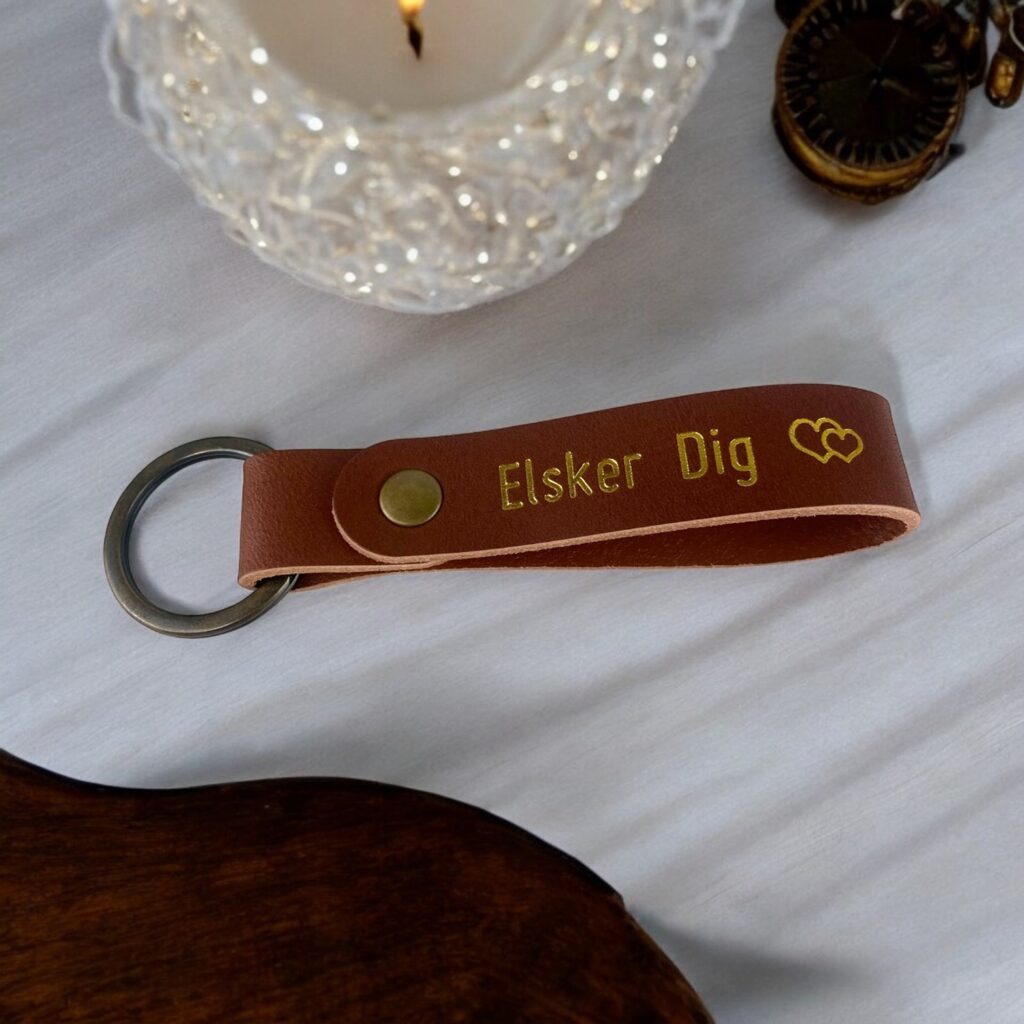 Cognac farvet lædernøglering med guldtekst. Der står Elsker Dig efterfulgt af et dobbelthjertesymbold.