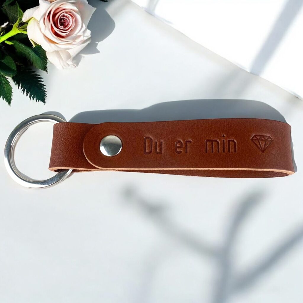 Bagsiden af en nøglering i cognac farvet læder. Der er trykt teksten Du er min efterfulgt af et diamant symbol.