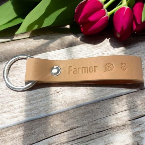 Nøglering i natur læder med personlig og sølv nitte. Der står Farmor og der er trykt to symboler. En firkløver og en blomst.