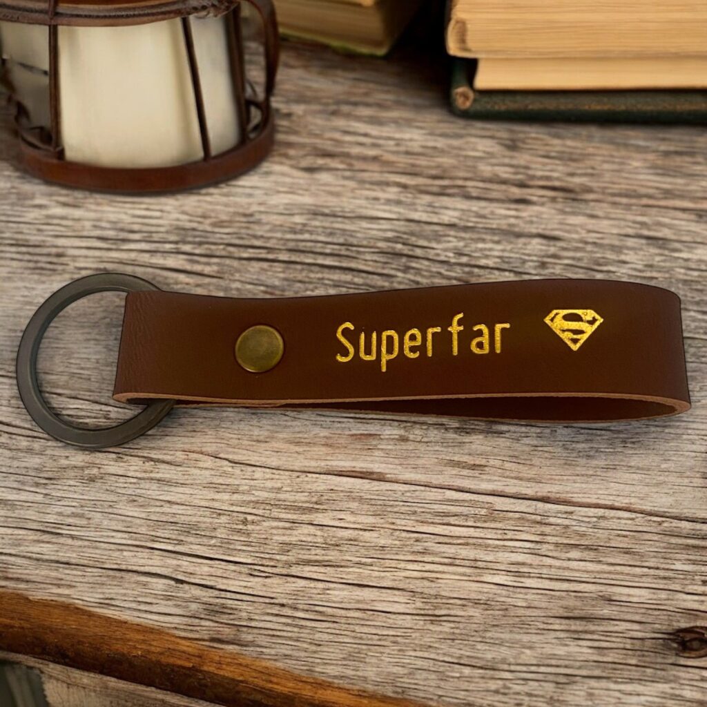 Cognac farvet nøglering i læder med teksten Superfar efterfulgt af et supermand symbol.