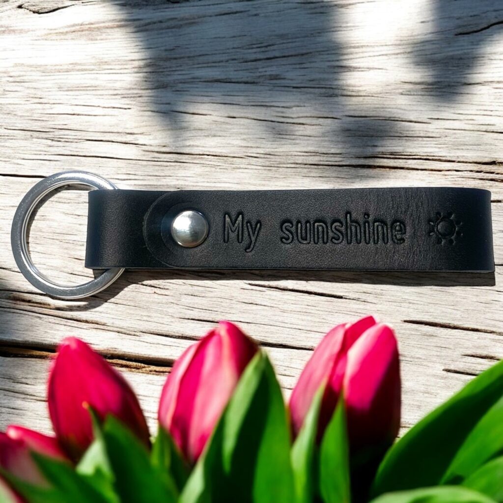 Nøglering i sort læder med tryk og sølv nøglering og nitte. Der står My Sunshine og har et symbol med en sol.