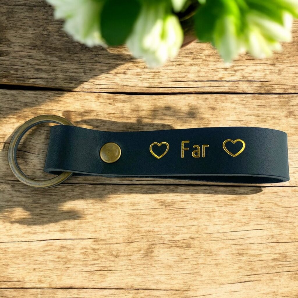 Sort nøglering i læder med guldskrift. Der står far med et hjerte på begge sider.