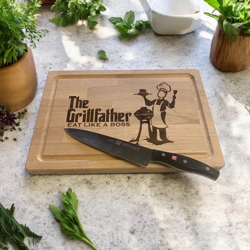 Skærebræt på bord med urter. På skærebrættet er graveret teksten: The Grillfather og der er en mand der står ed en grill.