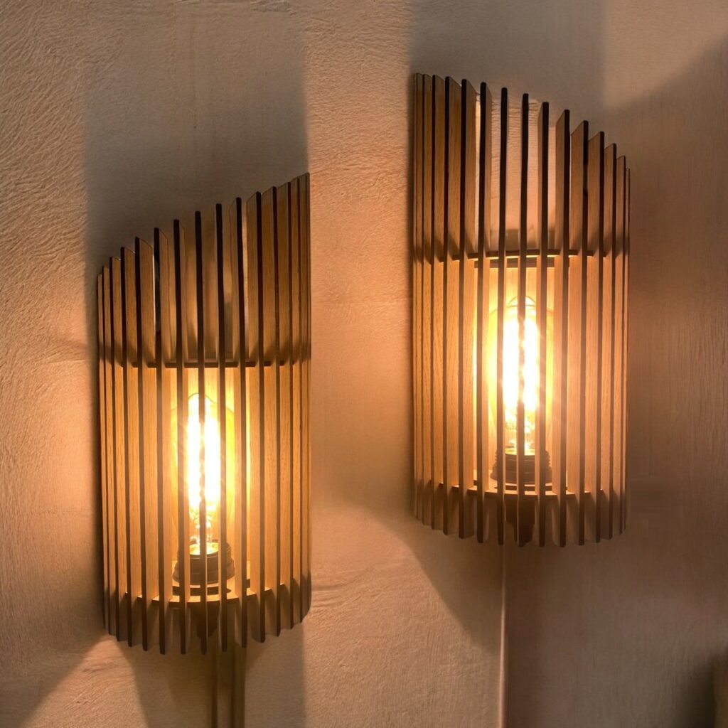 Twister væglamper i træ med lys i. To lamper med lameller som sidder lidt forskudt.