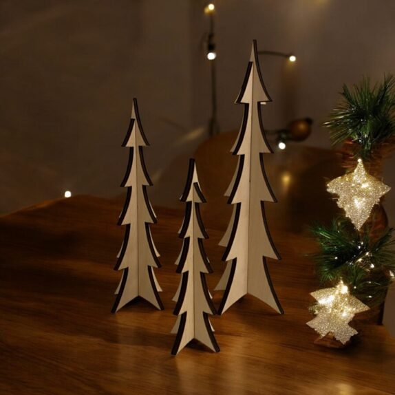 Tre juletræer i træ på et bord med julestemning og lys. Juletræerne har forskellige størrelser.